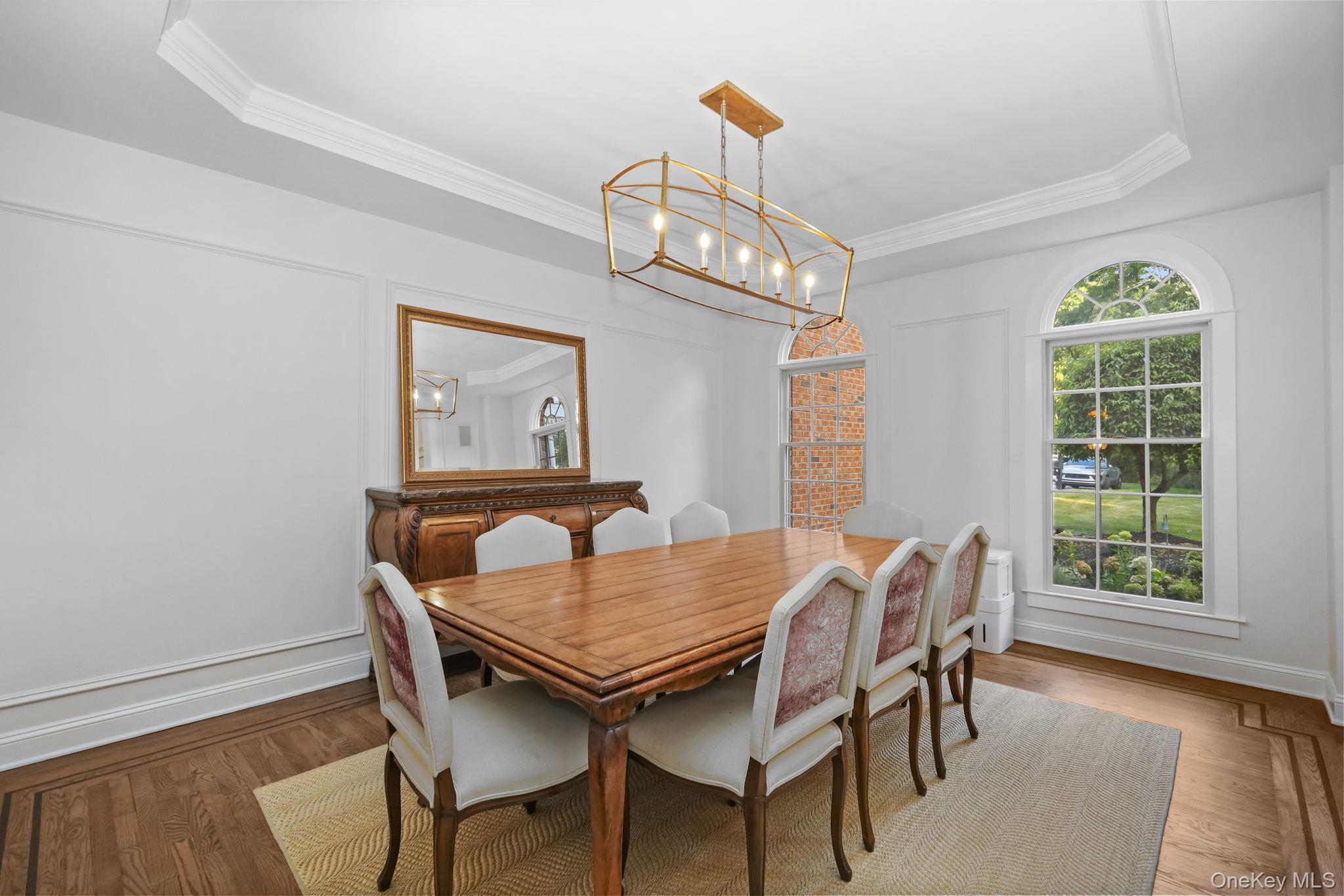 Dining room with a long wooden table, upholstered chairs, and tall arched windows.