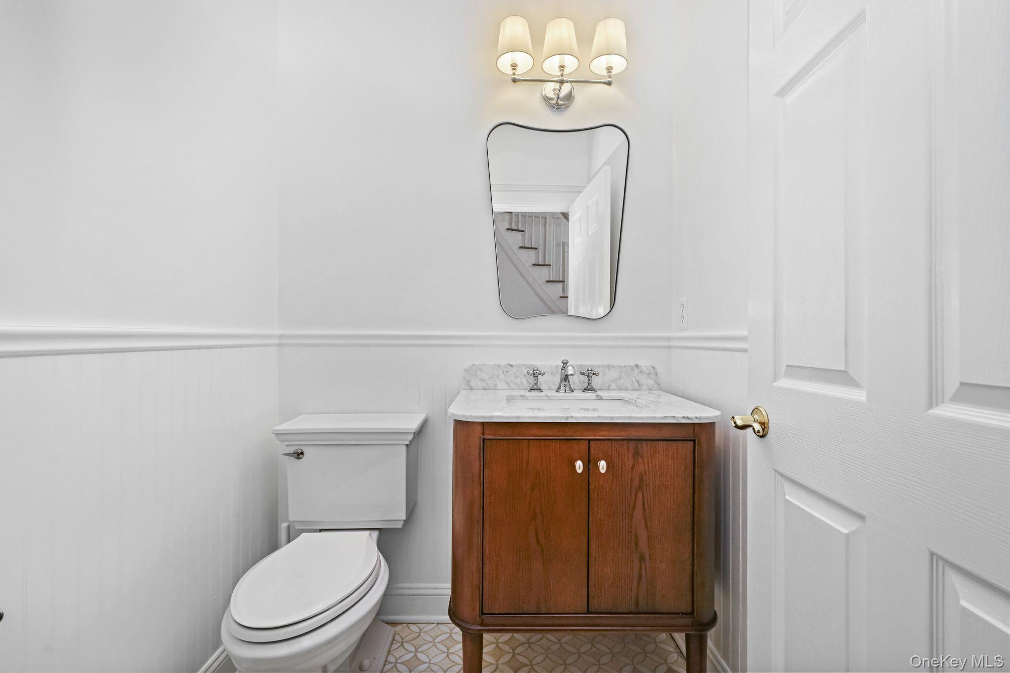 Bathroom with a dark wood vanity, marble countertop, and mirror reflecting a staircase.