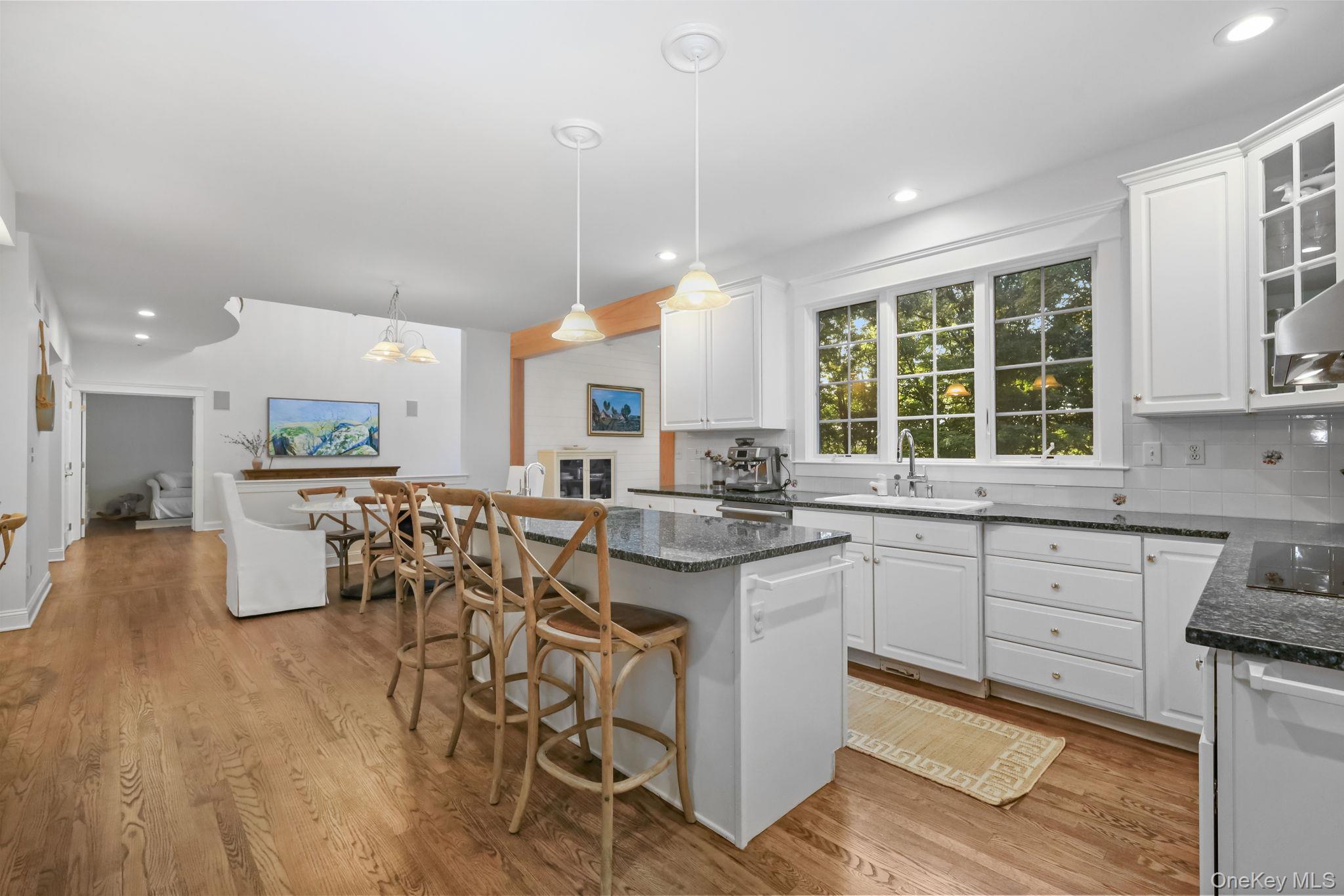 Bright white kitchen with a large stone island, bar seating, and hardwood floors.