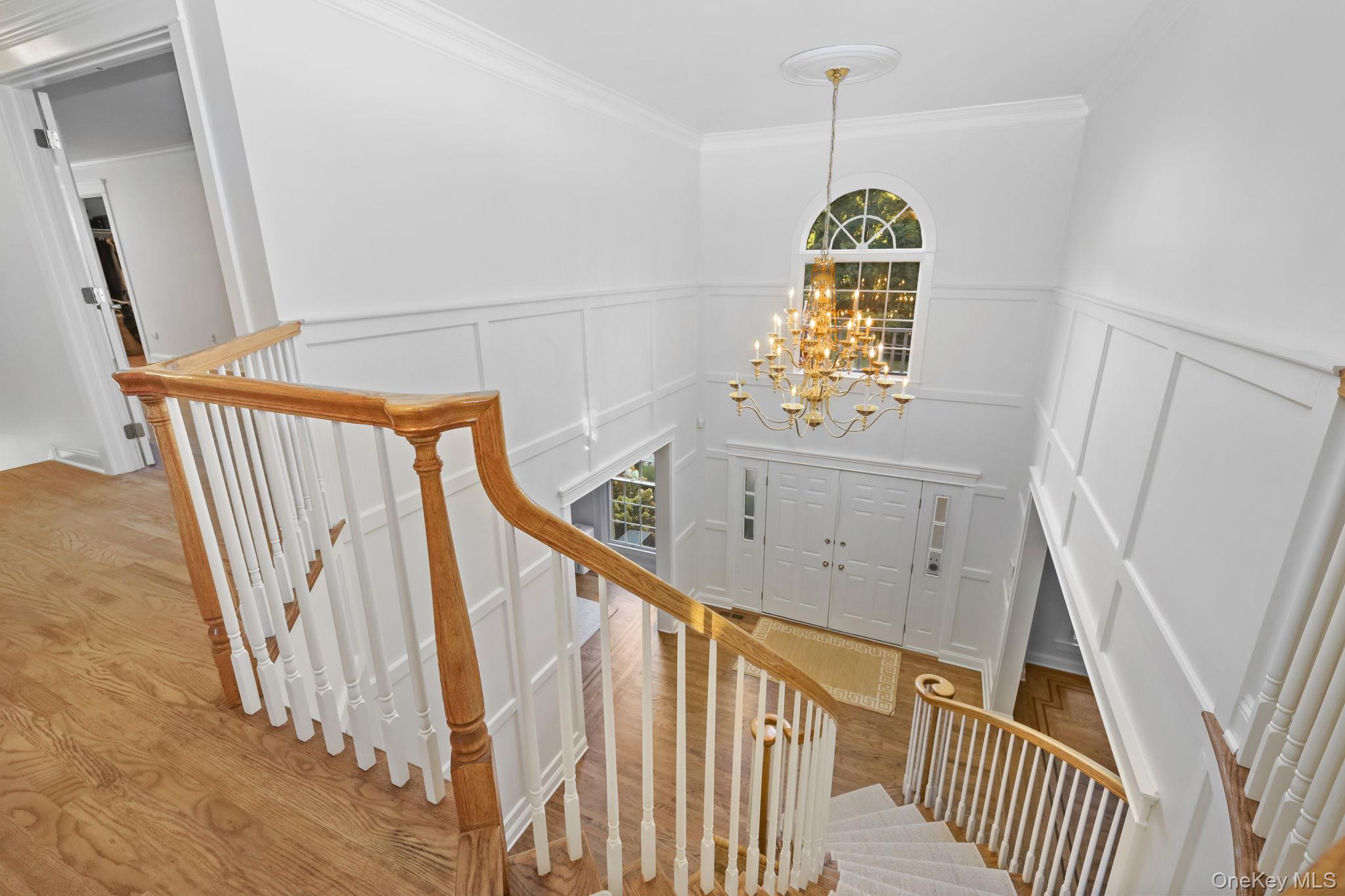 Two-story foyer with a curved staircase, hardwood floors, brass chandelier, and arched window above the front doors.