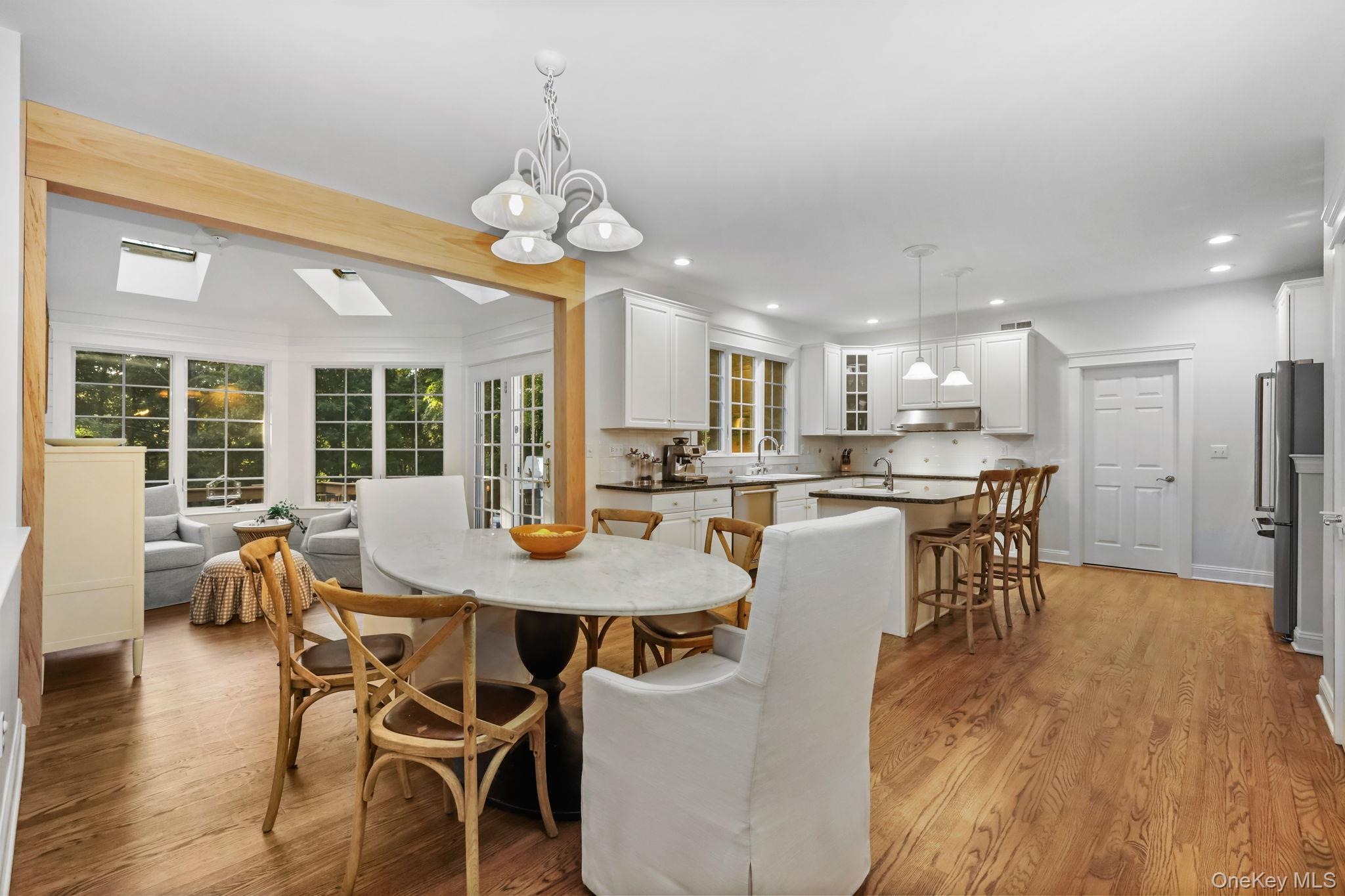 Open-plan kitchen and dining area with white cabinetry, a breakfast island, wood floors, and adjoining sitting area.