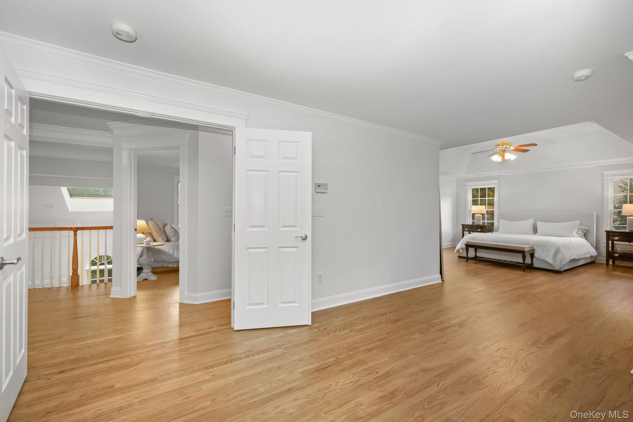 Bedroom with a white bed, wood ceiling fan, hardwood floors, and an open doorway to the landing.