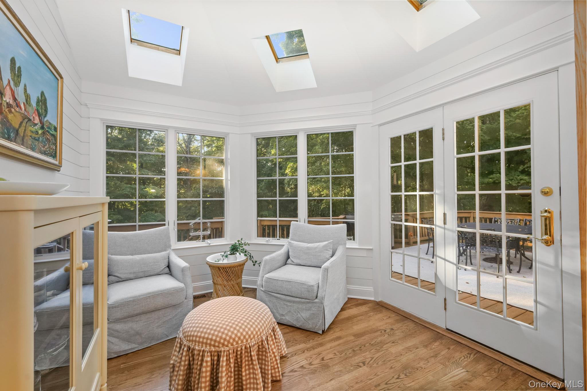 Bright sitting room with skylights, gray chairs, and French doors opening to a wooded deck.