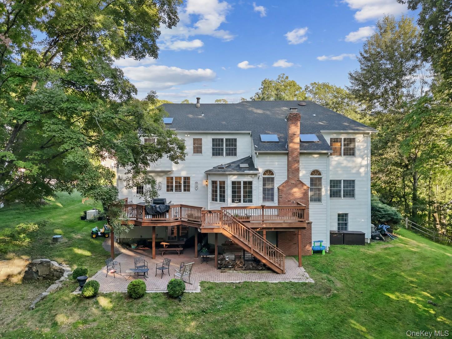 Rear of a white two-story house with a raised deck, brick chimney, and patio seating.