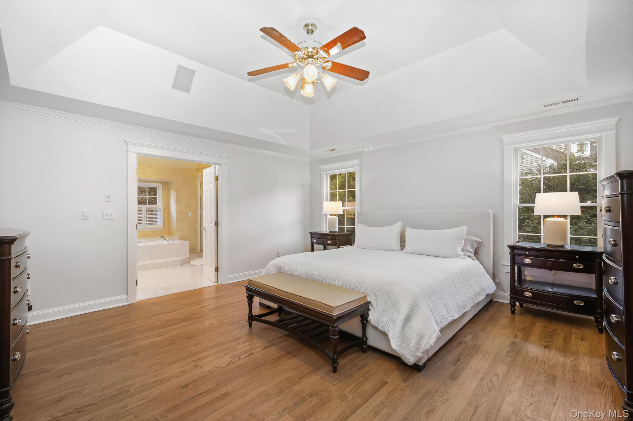 Bedroom with a white bed, hardwood floors, and an open doorway to an adjoining bathroom.