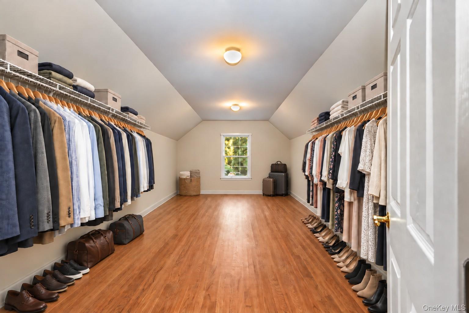 Walk-in closet with clothes and shoes lining both sides and a window at the far end.