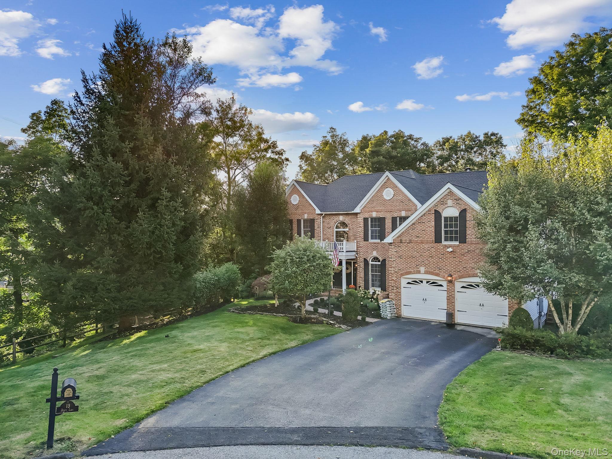 Two-story brick house with twin garage doors, a long driveway, and mature trees.