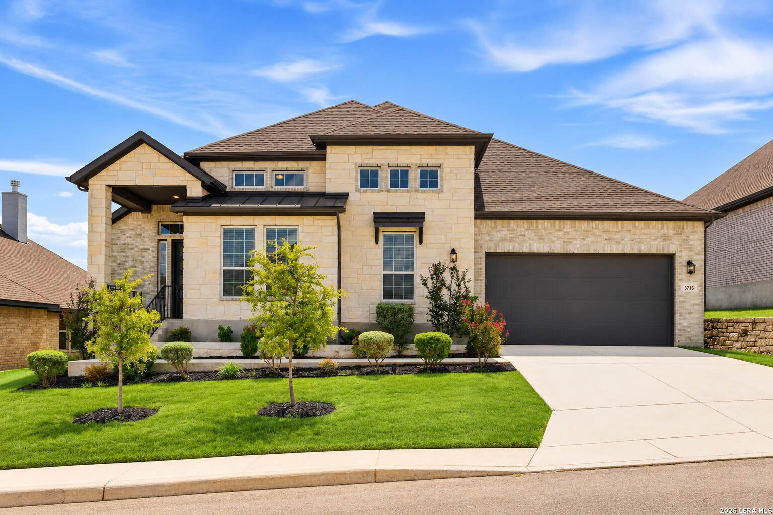 Two-story stone house with a covered entry, double garage, and landscaped front lawn.
