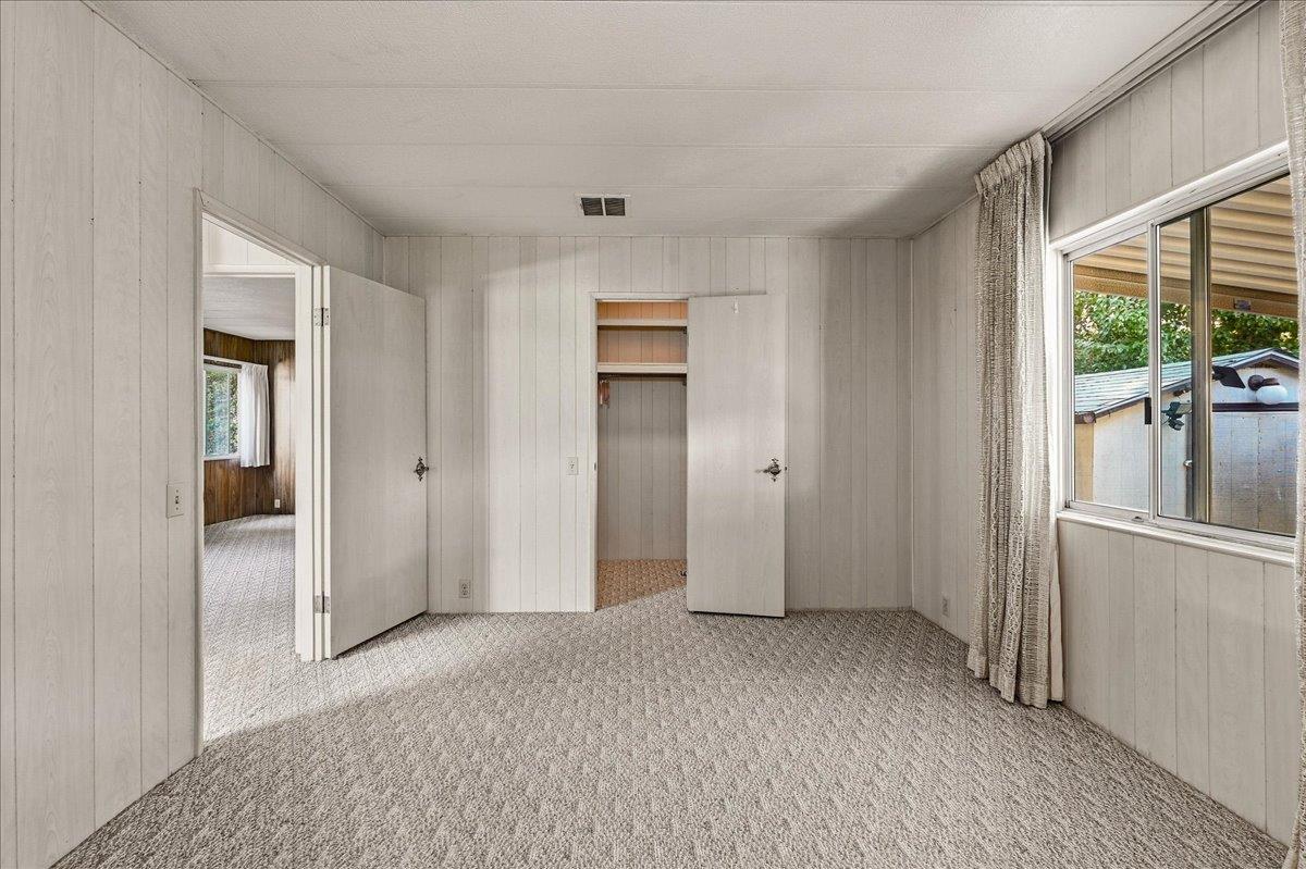 Empty bedroom with carpeted floor, paneled walls, open closet, and a large curtained window.
