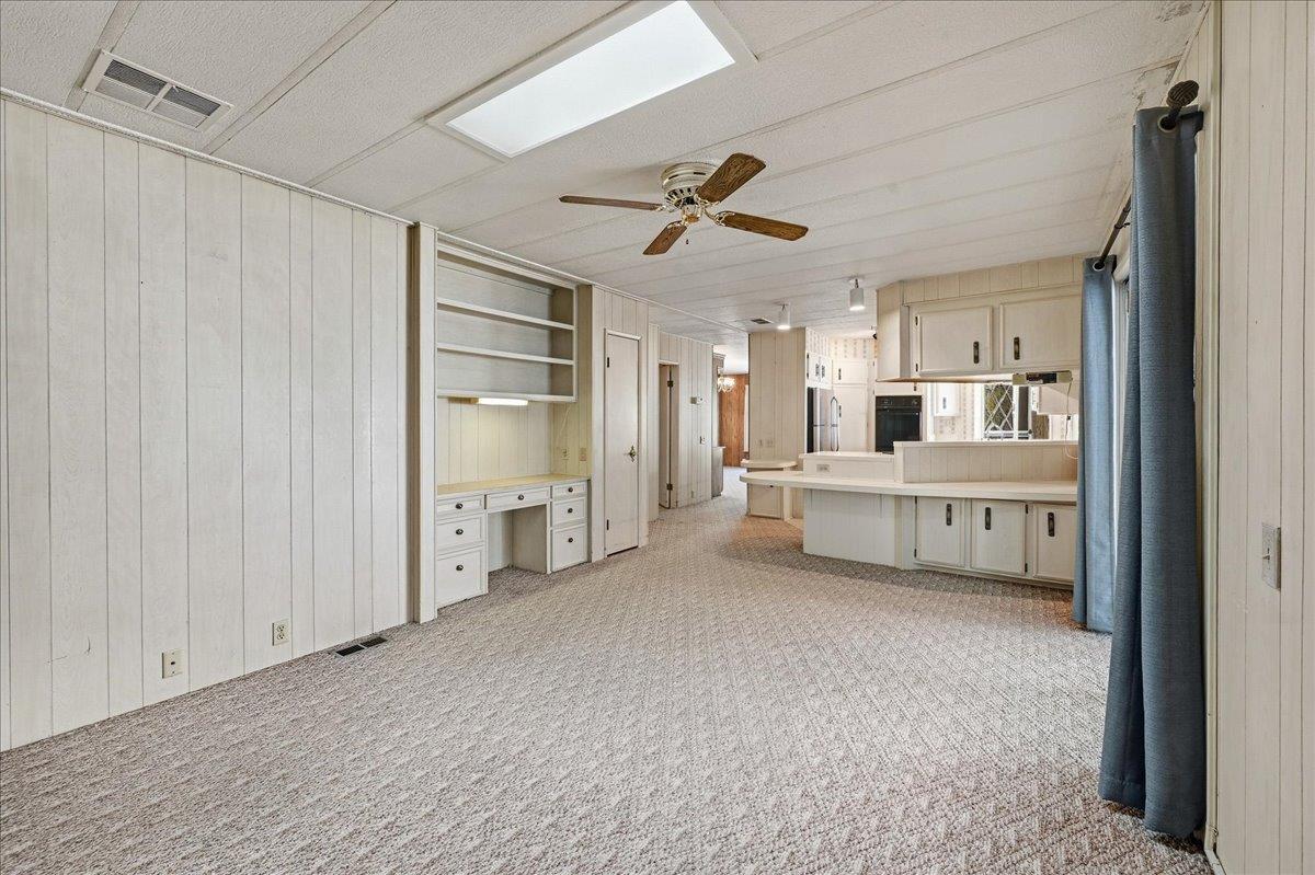 Unfurnished carpeted room opening into a kitchen, with built-in shelves and desk along one wall.