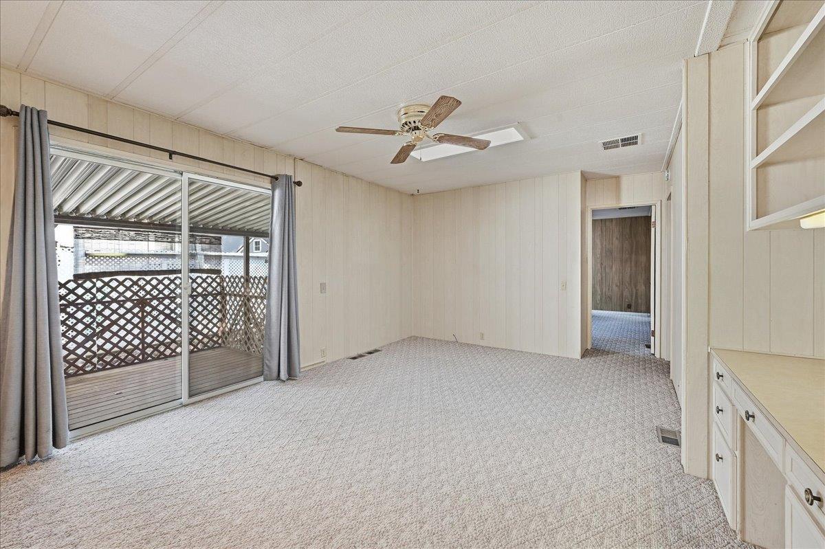 Empty carpeted room with sliding glass doors to a covered deck and built-in cabinetry.