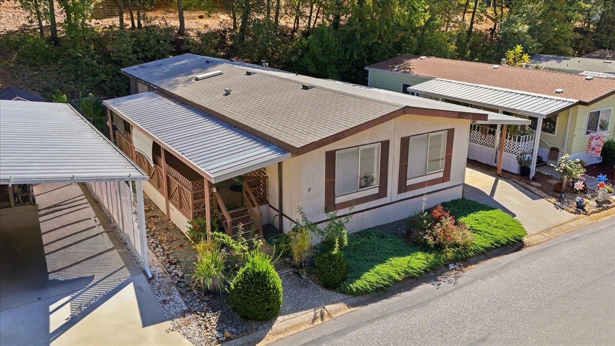 Single-story home with a covered carport, porch, landscaped yard, and wooded backdrop.