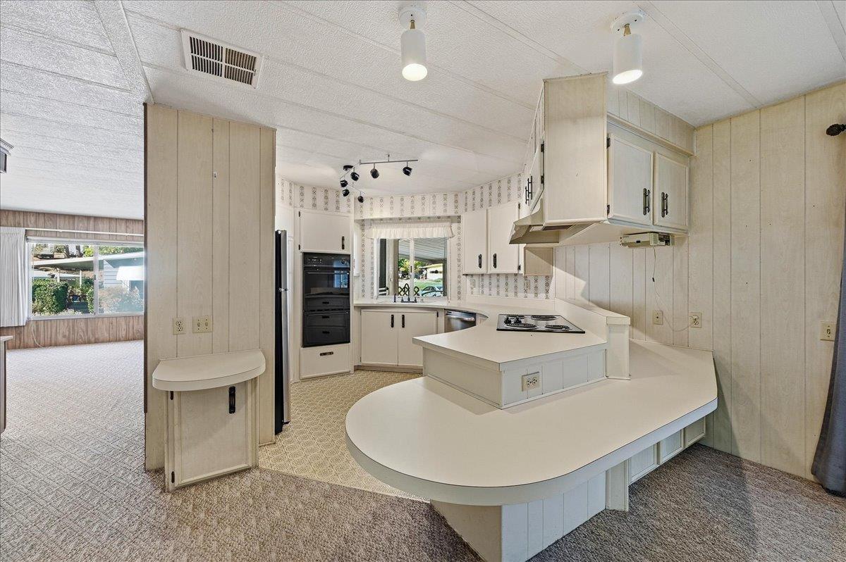 Kitchen with a large rounded white peninsula, cooktop, and built-in double ovens.