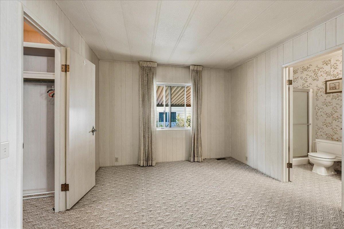 Empty carpeted bedroom with an open closet and an adjoining bathroom.