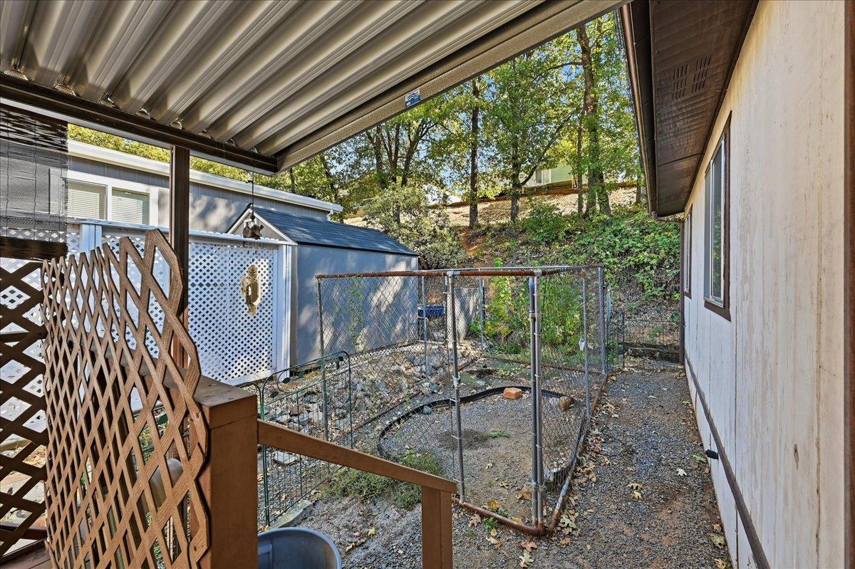 Covered patio overlooking a gravel side yard with a fenced dog run and trees.