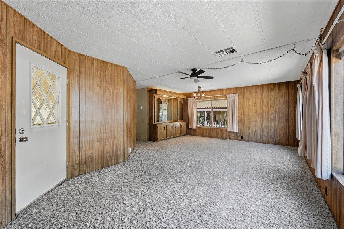 Vacant living room with wood-paneled walls, gray carpet, and a built-in wooden hutch.