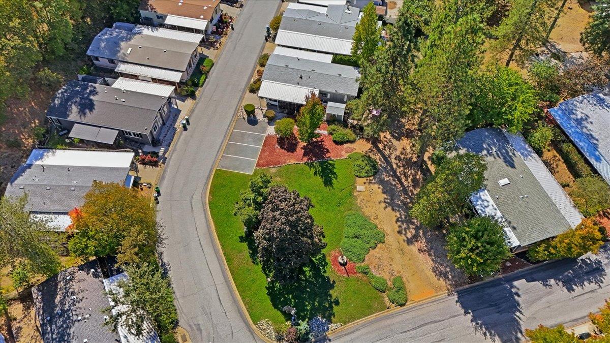Aerial view of homes along a curved street beside a landscaped lawn and mature trees.