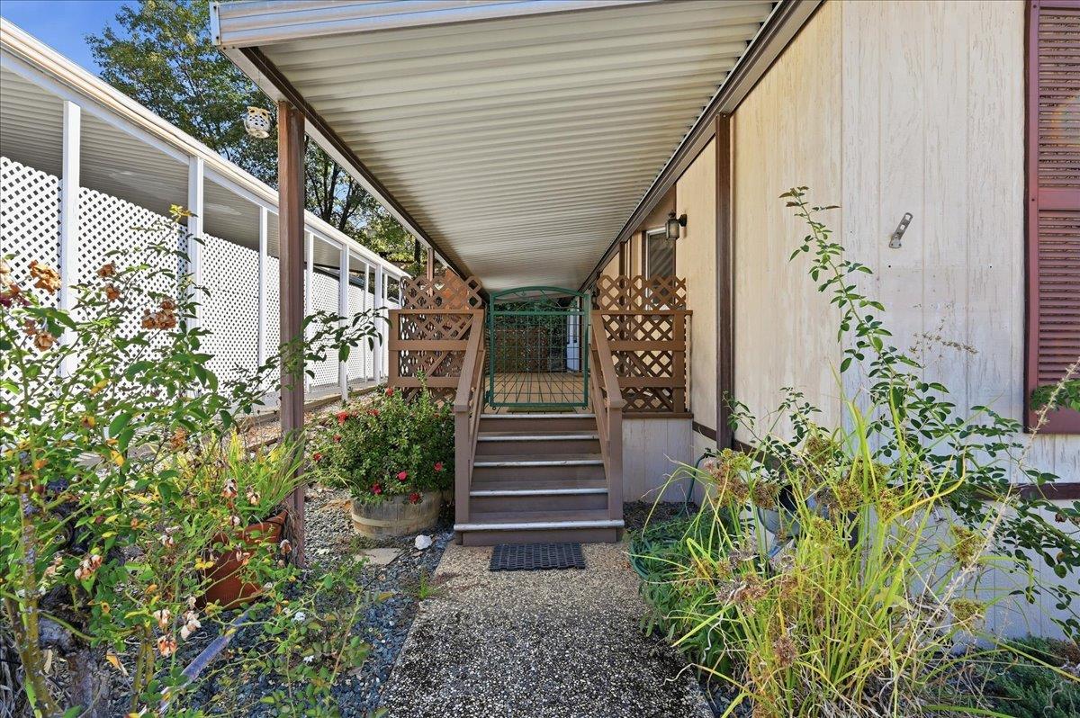 Covered home entry with steps to a gated landing, bordered by flowering planters and white lattice fencing.