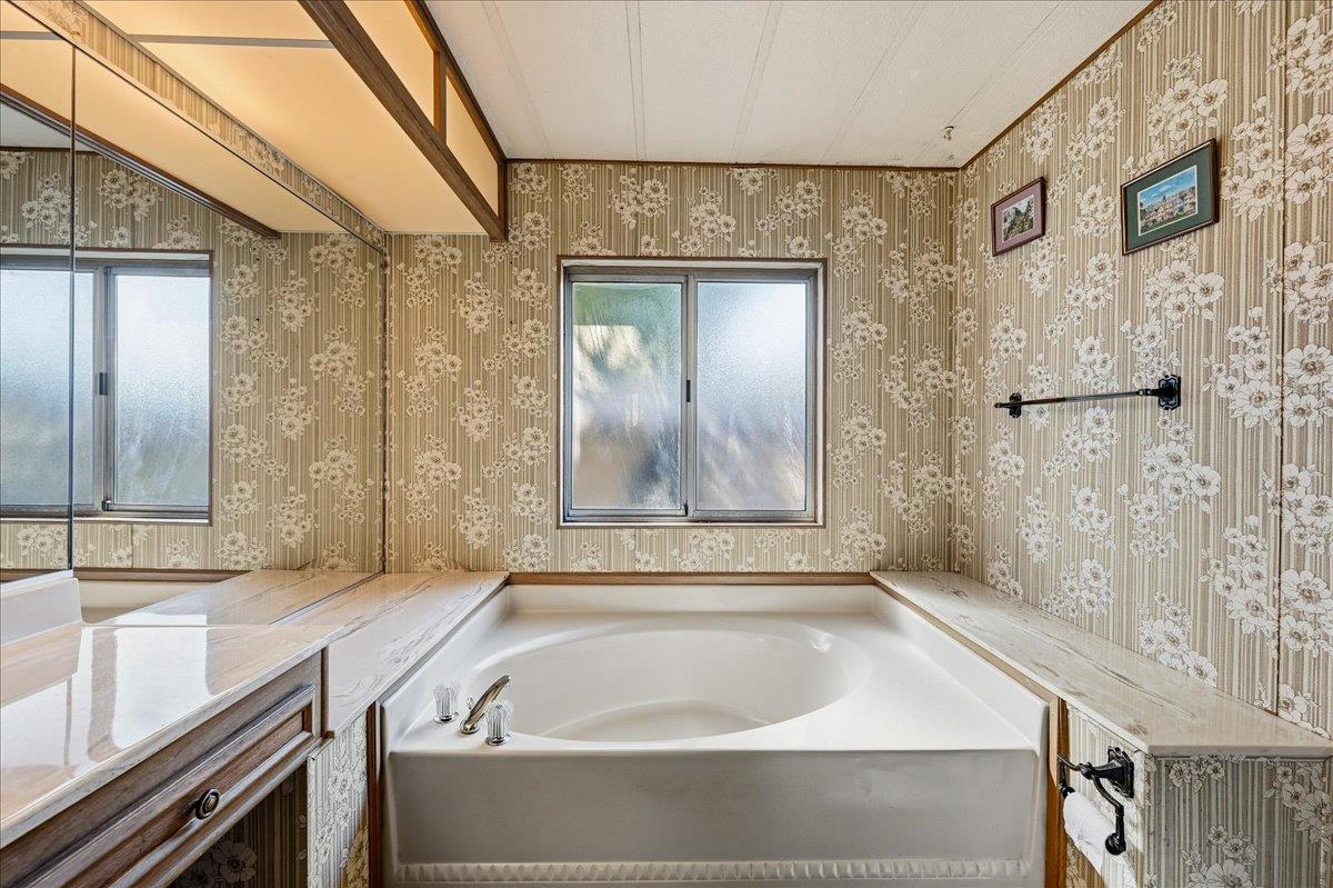Bathroom with a corner soaking tub, marble-look counters, and floral wallpaper.