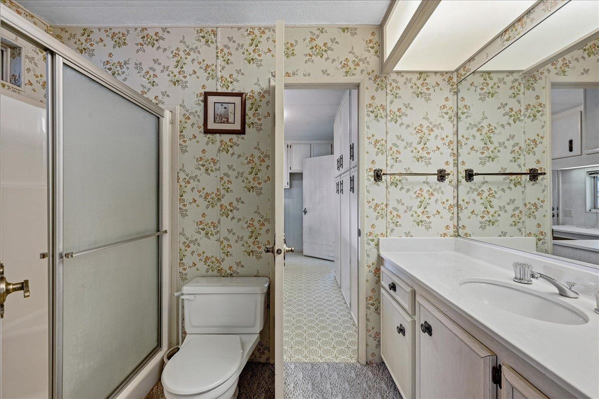 Bathroom with floral wallpaper, frosted-glass shower, toilet, and long white vanity.