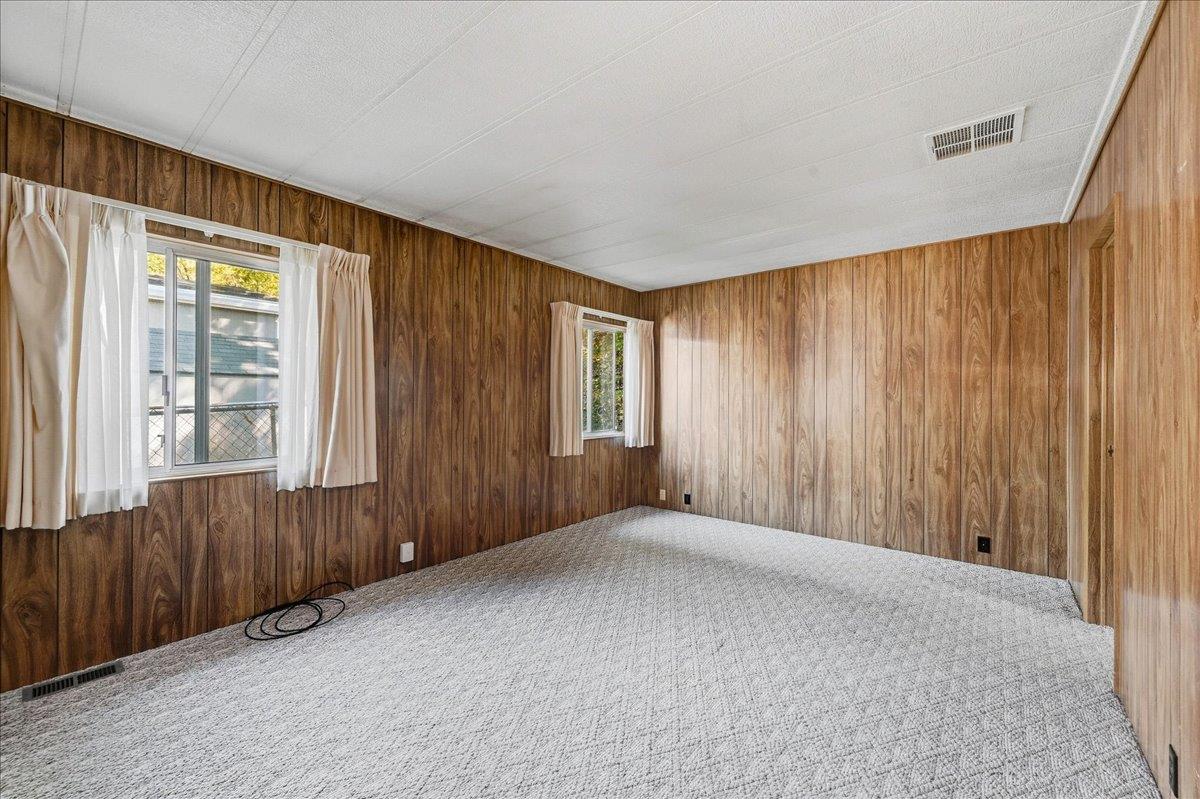 Empty bedroom with wood-paneled walls, gray carpet, and two curtained windows.