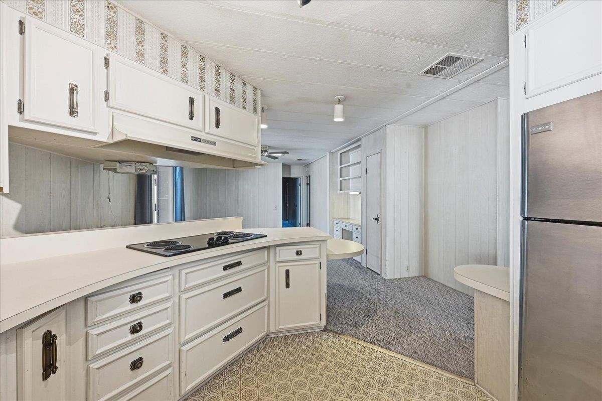White kitchen with a built-in cooktop, stainless steel refrigerator, and patterned floor.