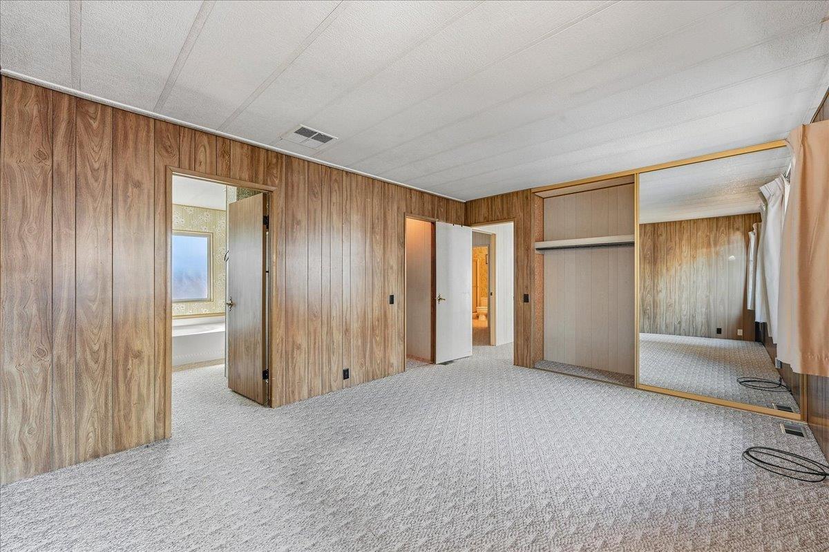 Empty bedroom with wood-paneled walls, carpet, and mirrored sliding closet doors.