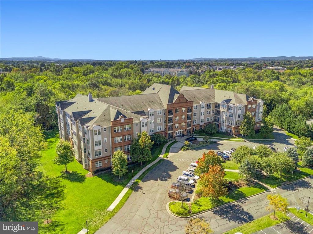 Aerial view of a multi-story residential building surrounded by trees, lawns, and parking areas.