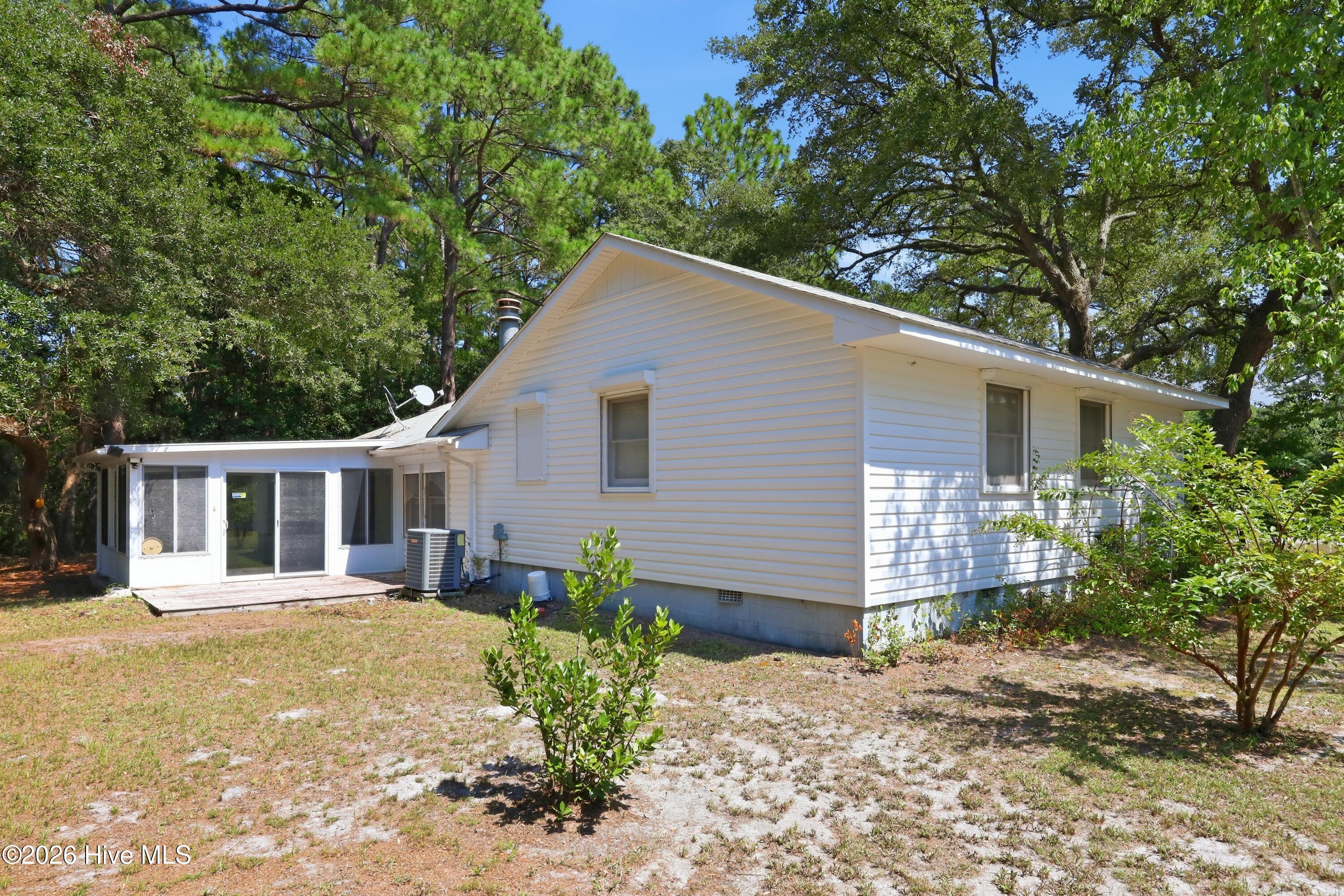 White-sided house with an attached screened sunroom and small deck, surrounded by mature trees.