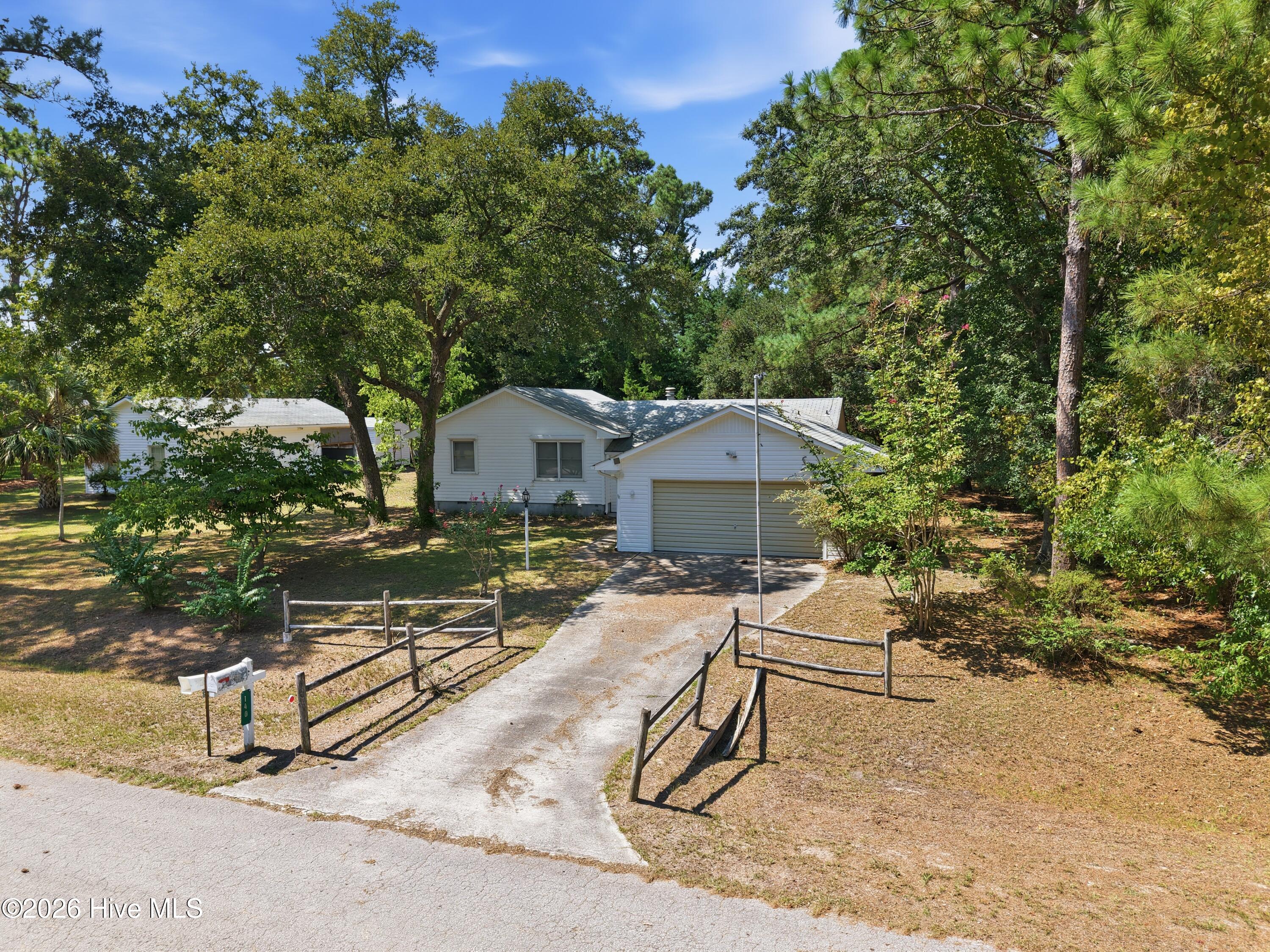White single-story house with attached garage, long driveway, and mature trees.