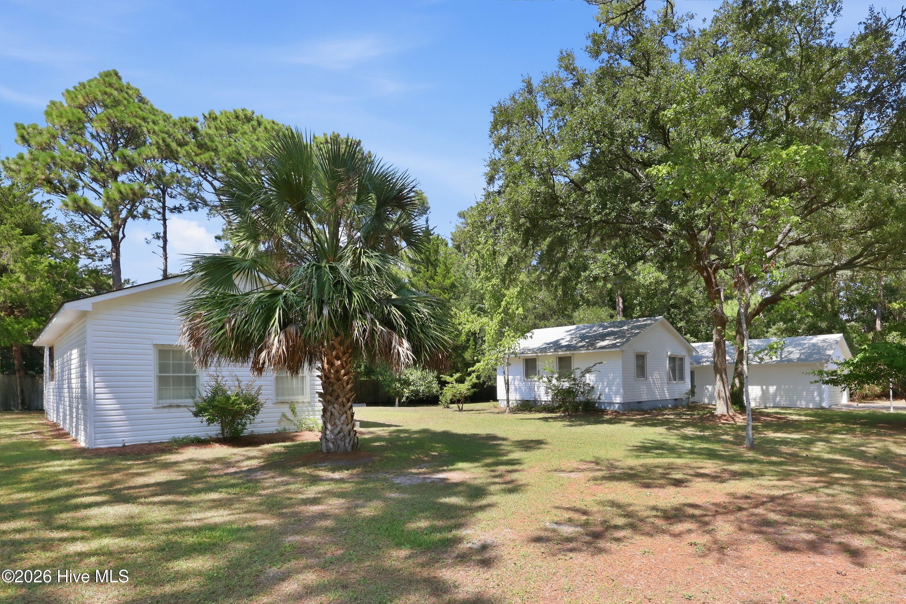White single-story home with a detached garage, palm tree, and mature trees across a broad yard.