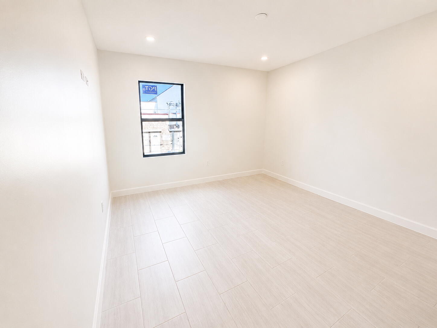 Empty bedroom with pale tile flooring and a single black-framed window.