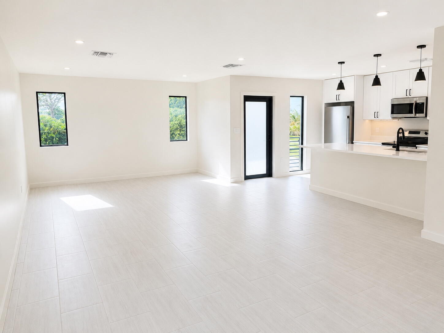 Vacant open-plan living area and kitchen with pale tile floors, white cabinetry, and stainless steel appliances.
