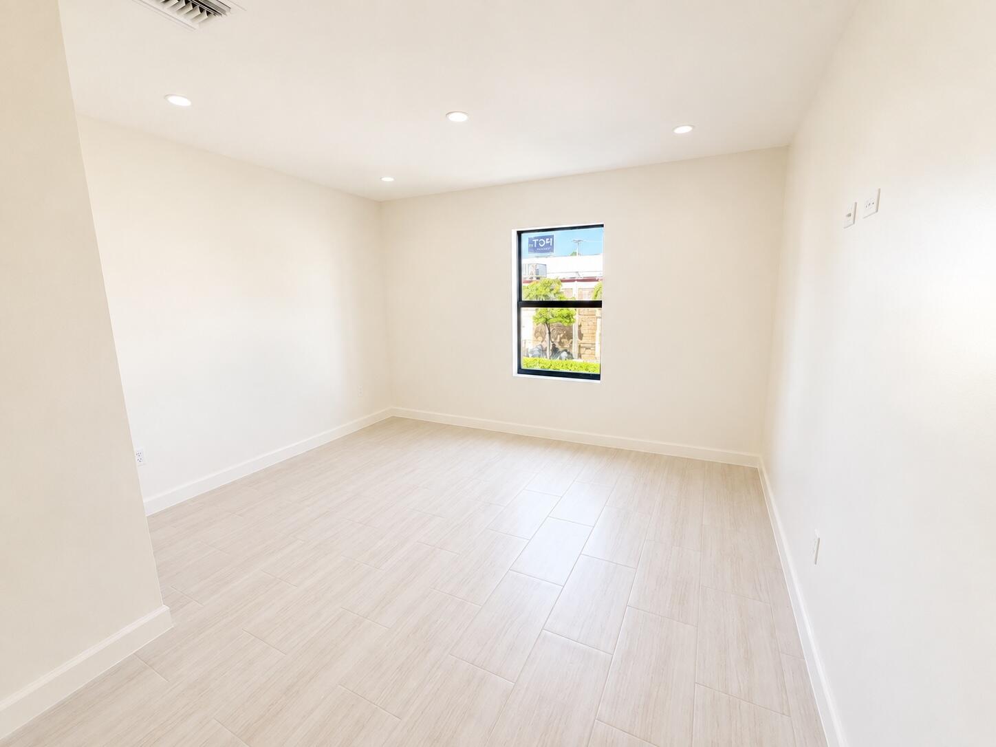 Vacant room with pale tile flooring, recessed lights, and a window overlooking greenery.