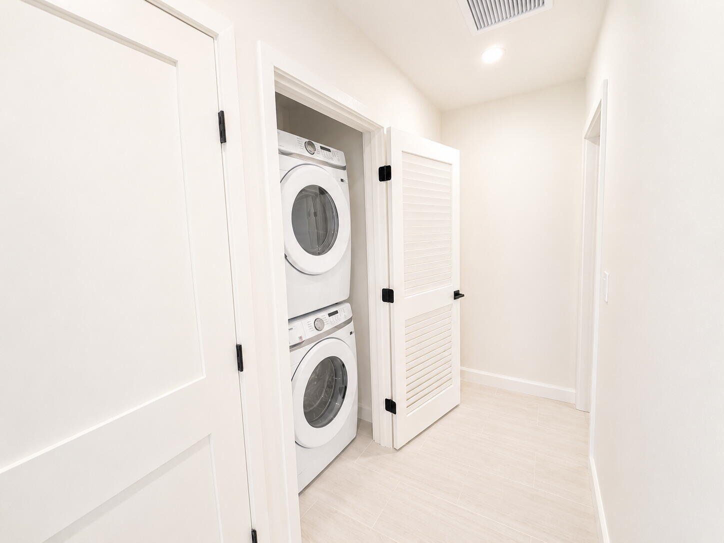 Laundry closet with stacked front-loading washer and dryer and open louvered doors.