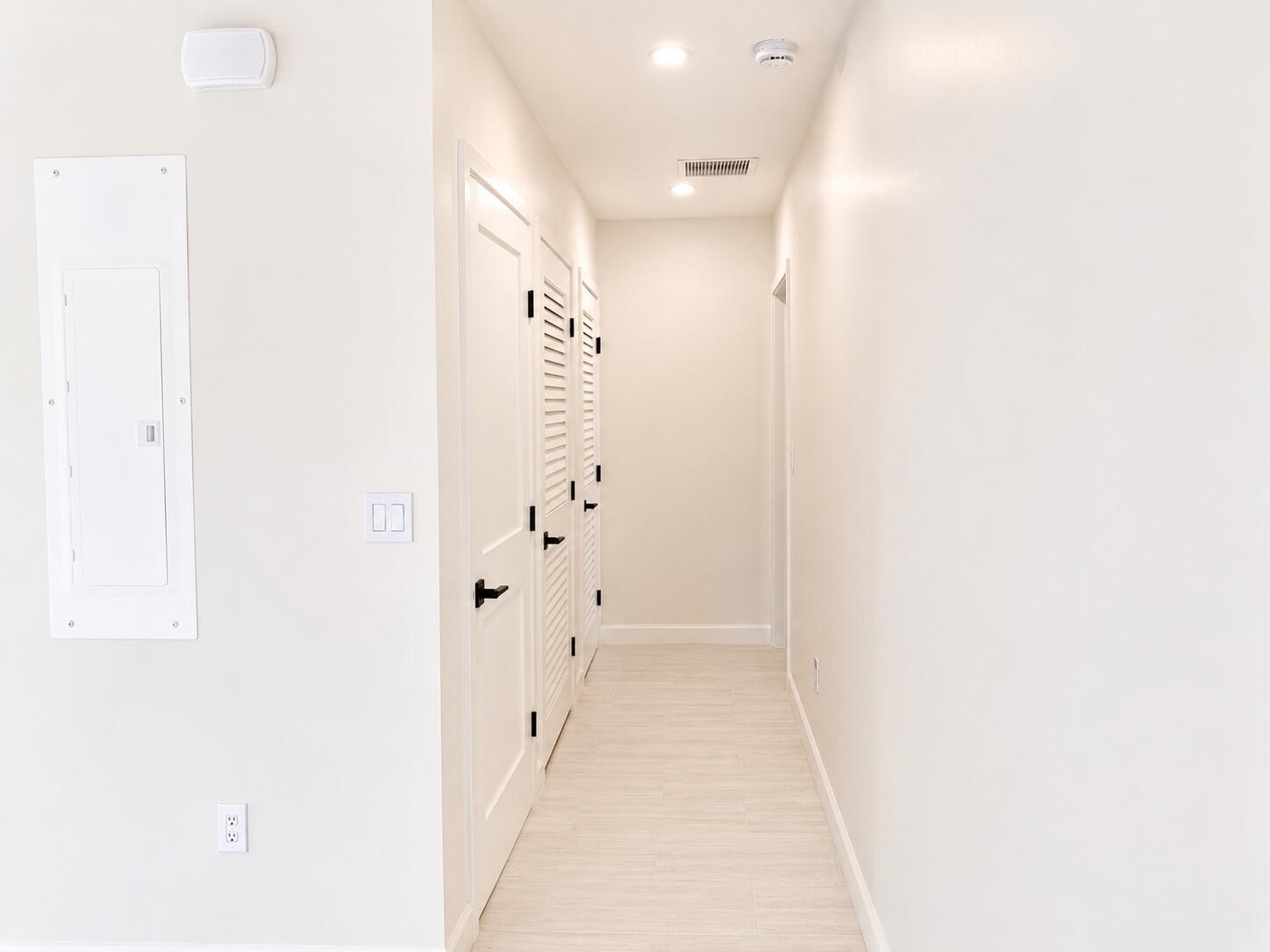 Bright white hallway with pale tile flooring and several doors with black hardware.