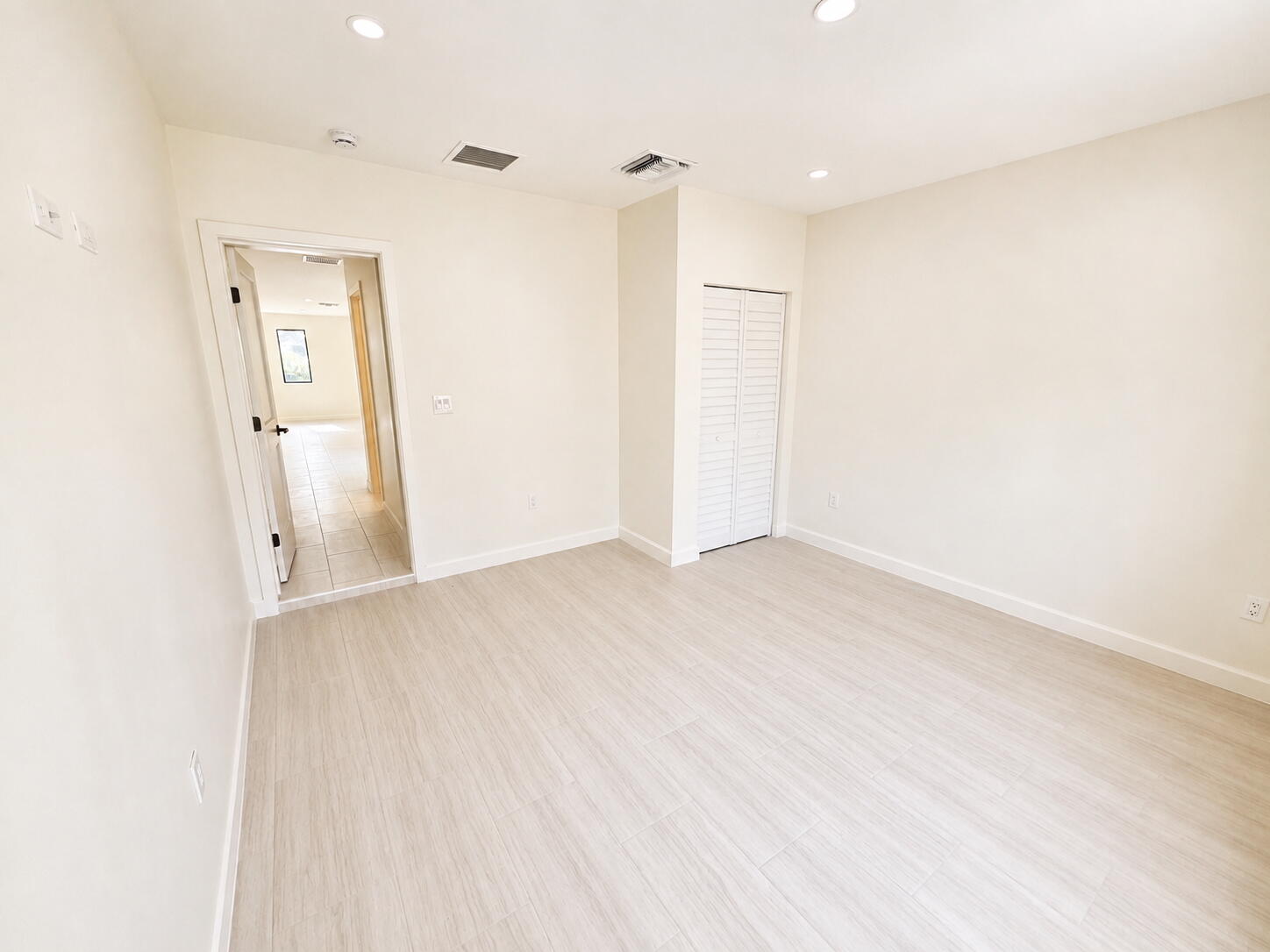 Empty bedroom with pale tile flooring, recessed lights, and a louvered closet.