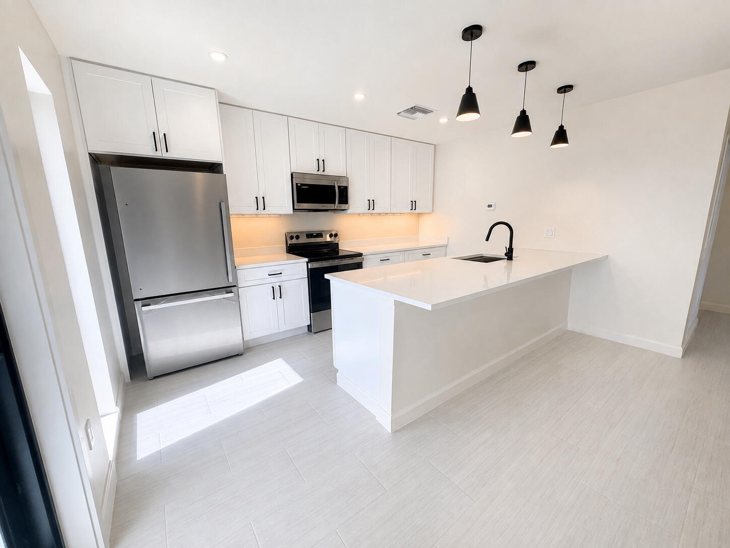 Bright kitchen with white cabinets, stainless steel appliances, and a large island beneath pendant lights.