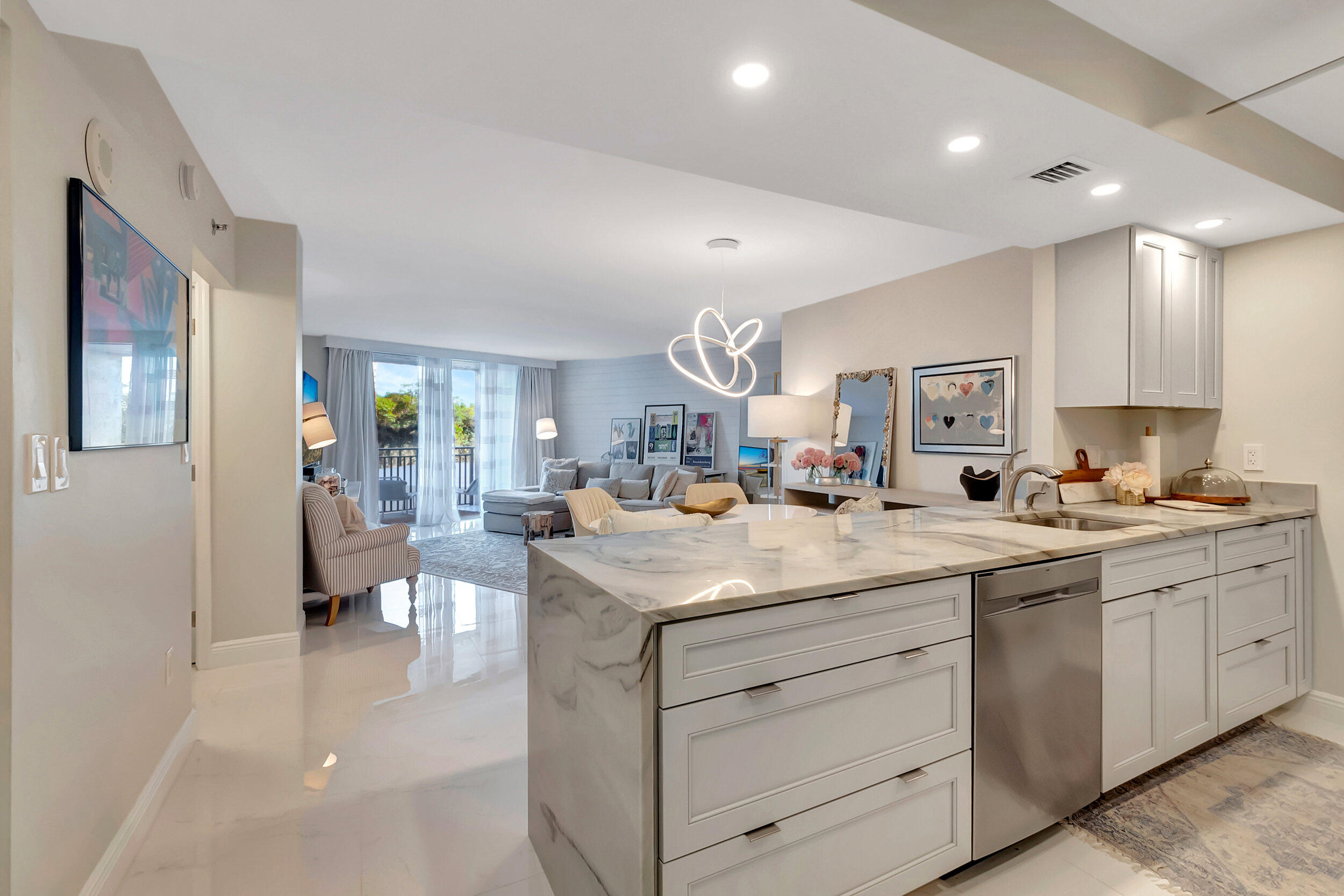 Open-plan condo kitchen with a marble island overlooking a furnished living room and balcony doors.