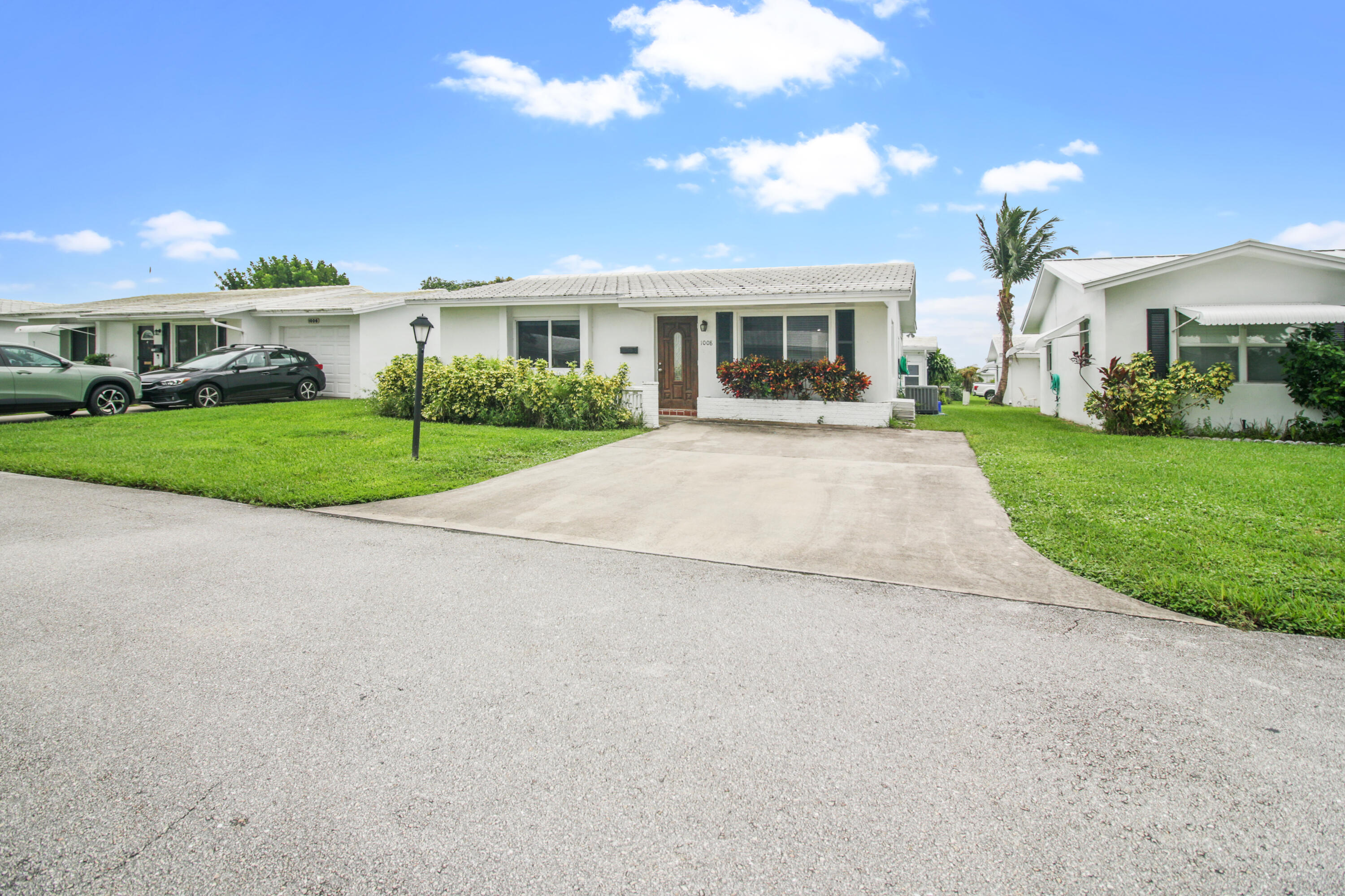 Single-story white house with front shrubs, green lawn, and a wide concrete driveway.