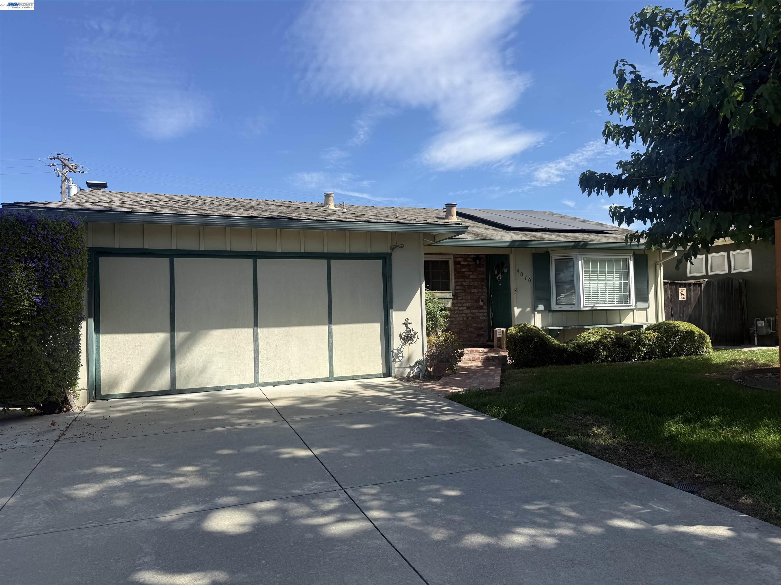 Single-story home with a wide two-car garage, rooftop solar panels, and a landscaped front yard.