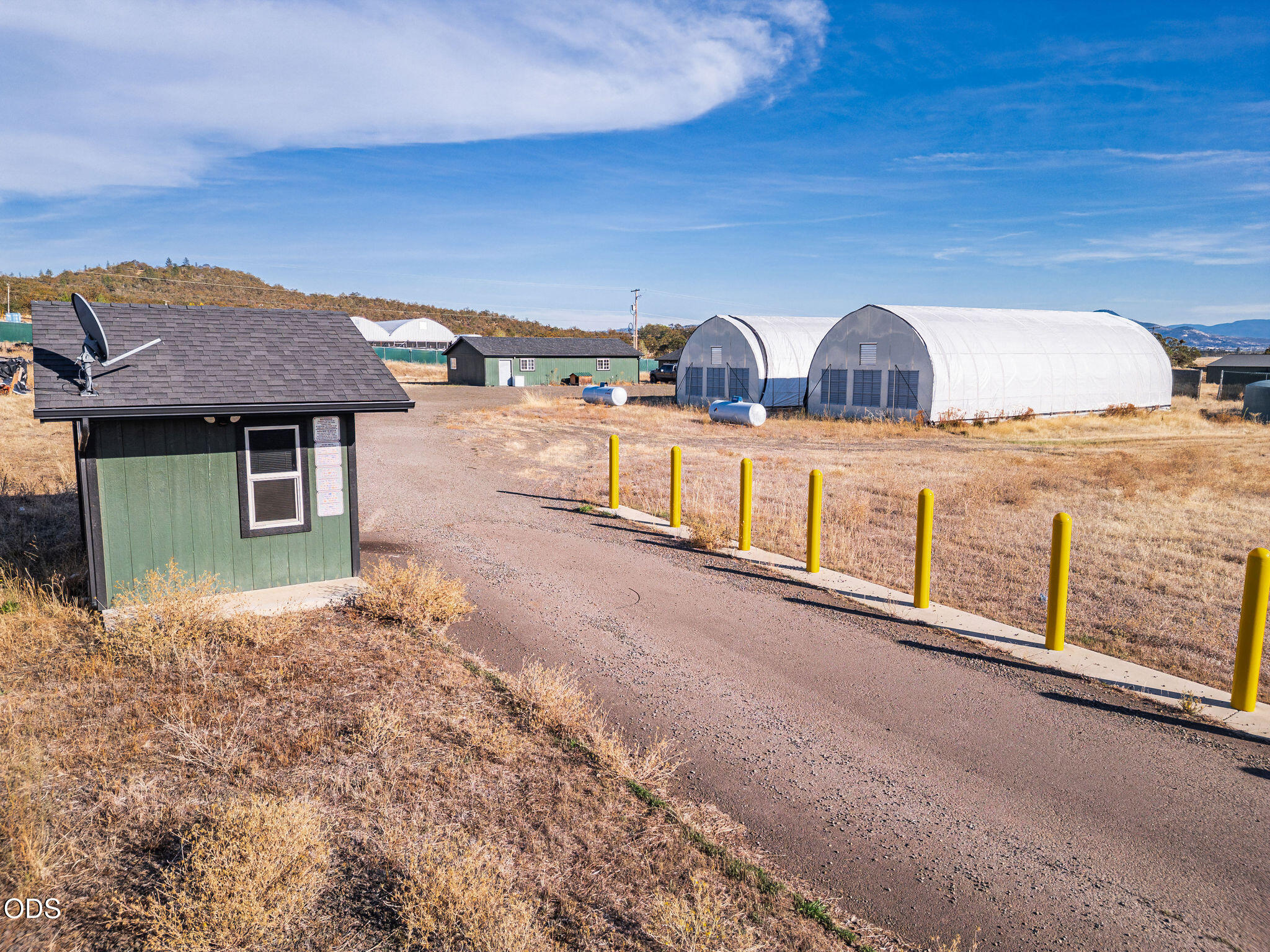 Property grounds with greenhouse buildings, a small office, and yellow bollards lining the driveway.