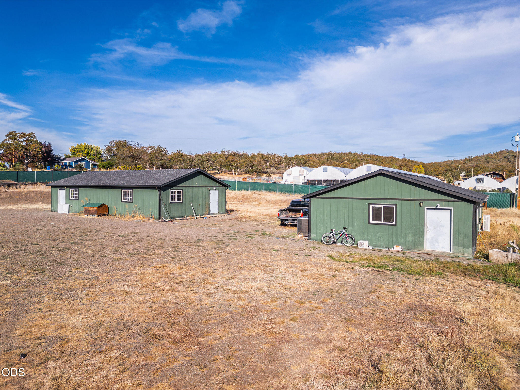 Two green outbuildings on a dry lot, with a bicycle beside the nearer building.