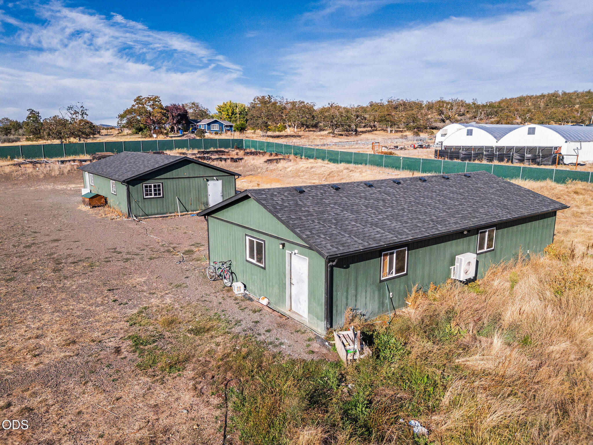 Aerial view of two green buildings on a dry lot, with white hoop barns behind.