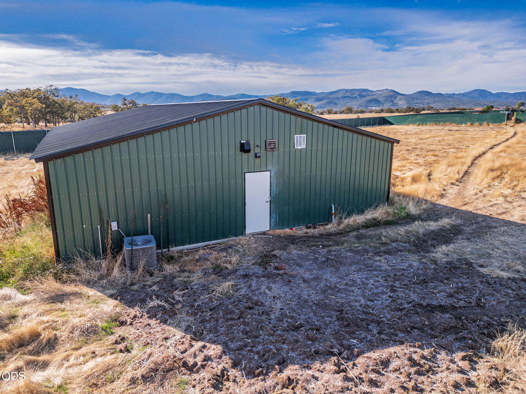 Green metal outbuilding with a white door in dry grassland, backed by distant mountains.