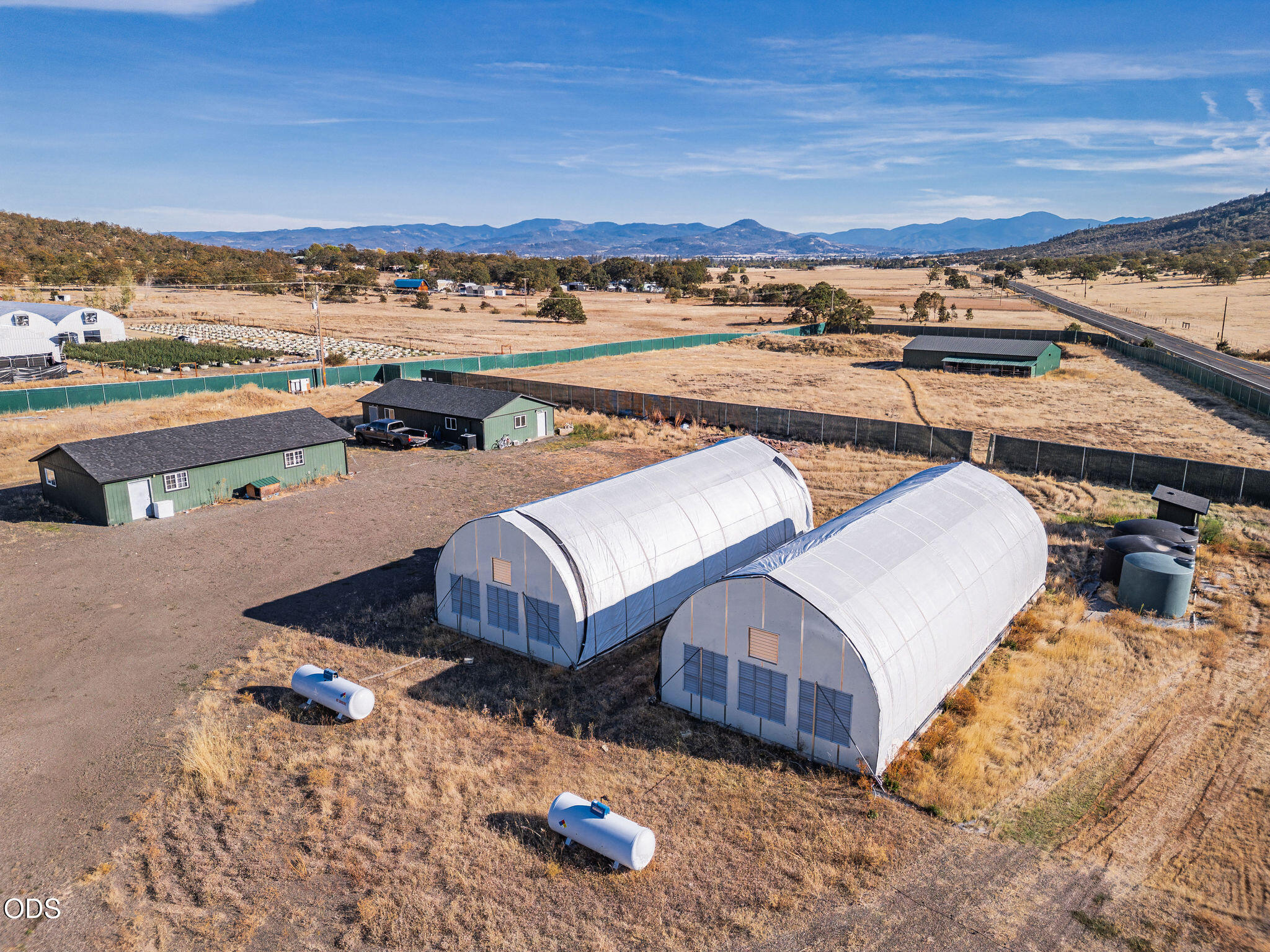 Aerial view of two white hoop houses and green outbuildings on a fenced rural property.