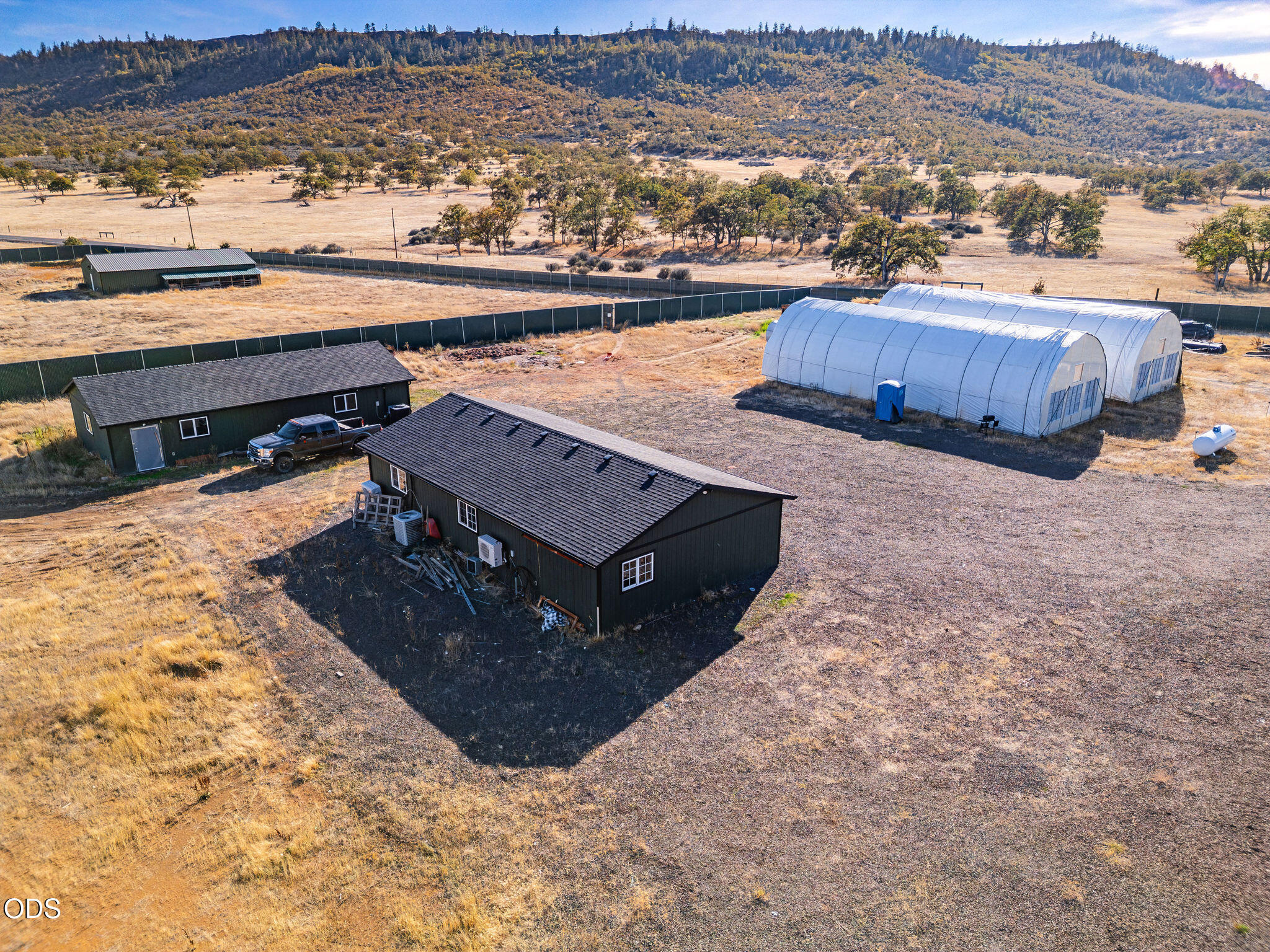 Aerial view of a rural property with two dark outbuildings and two white hoop greenhouses.