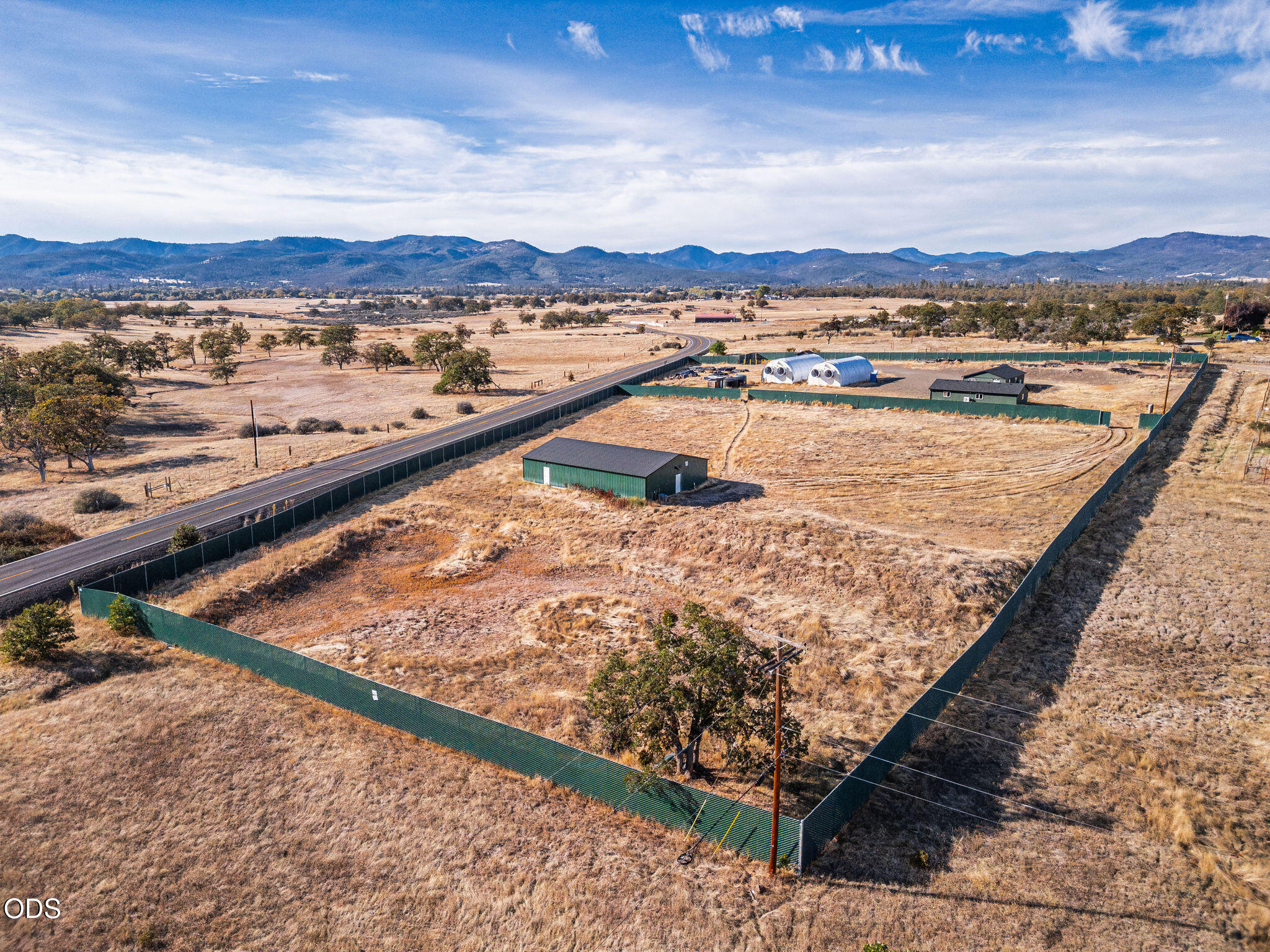 Fenced rural acreage with outbuildings, hoop structures, and mountain ridges beyond.