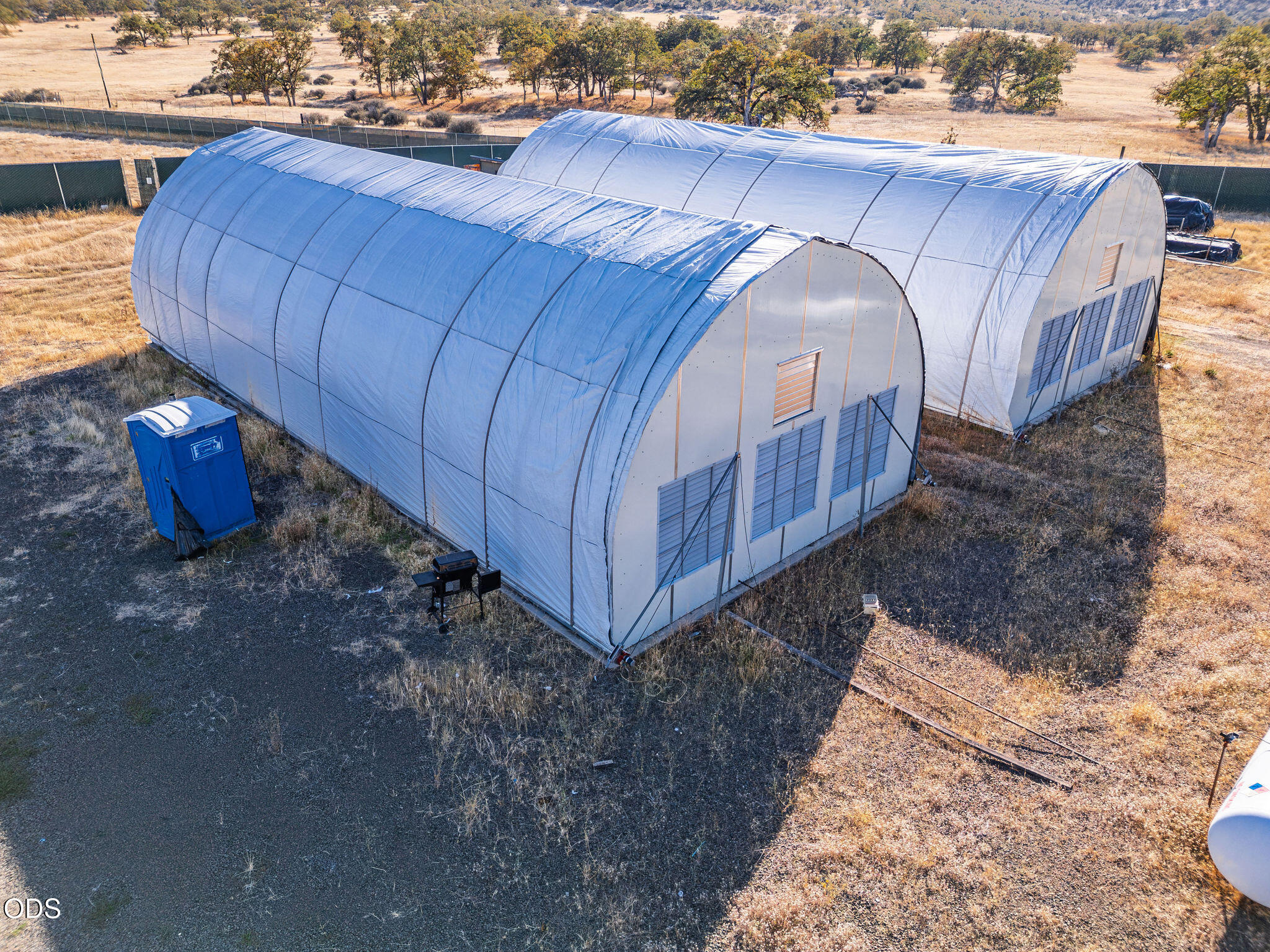 Two white fabric-covered hoop buildings stand on dry rural acreage.