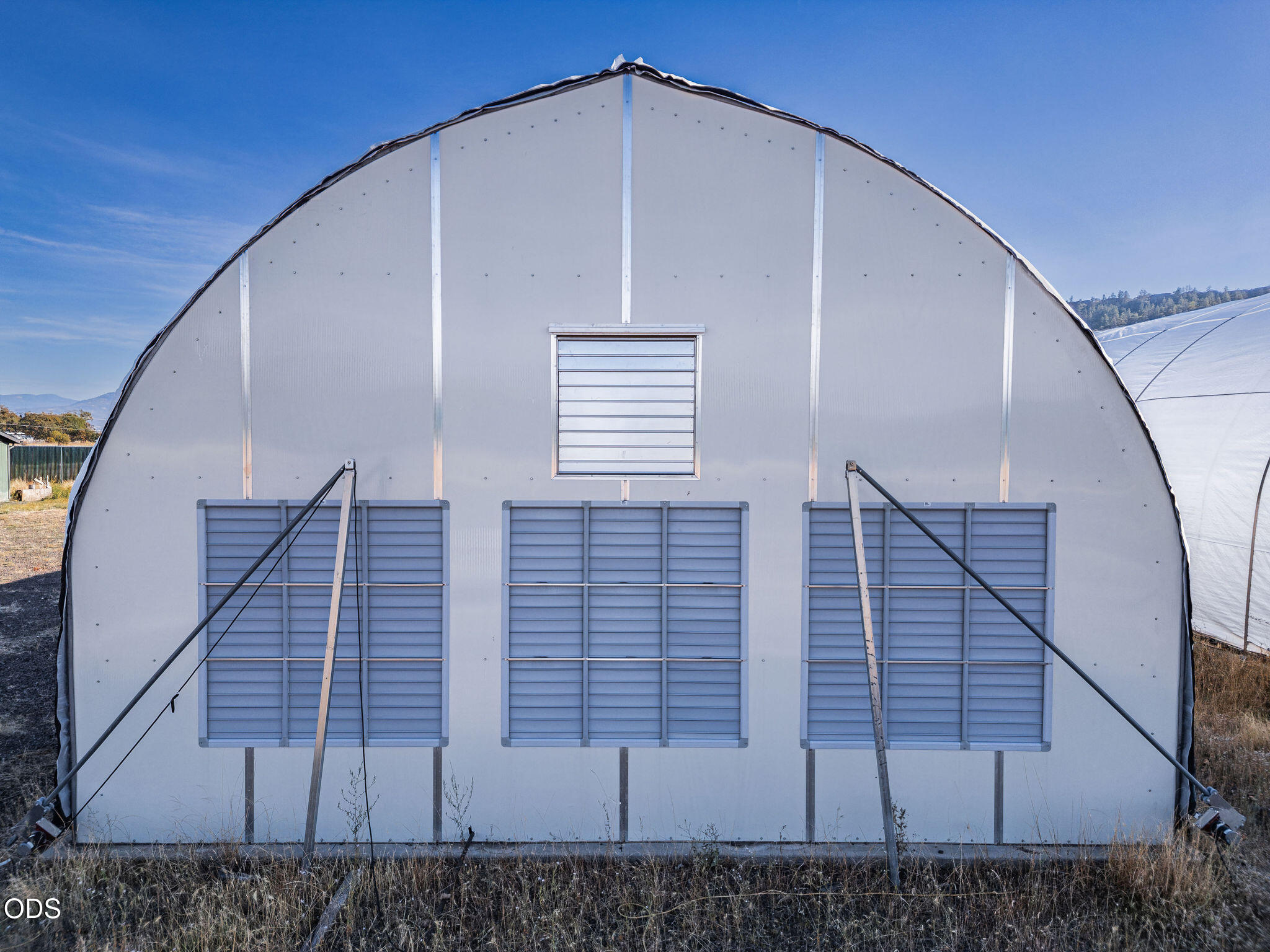 White Quonset-style outbuilding with three louvered panels and a small upper vent.